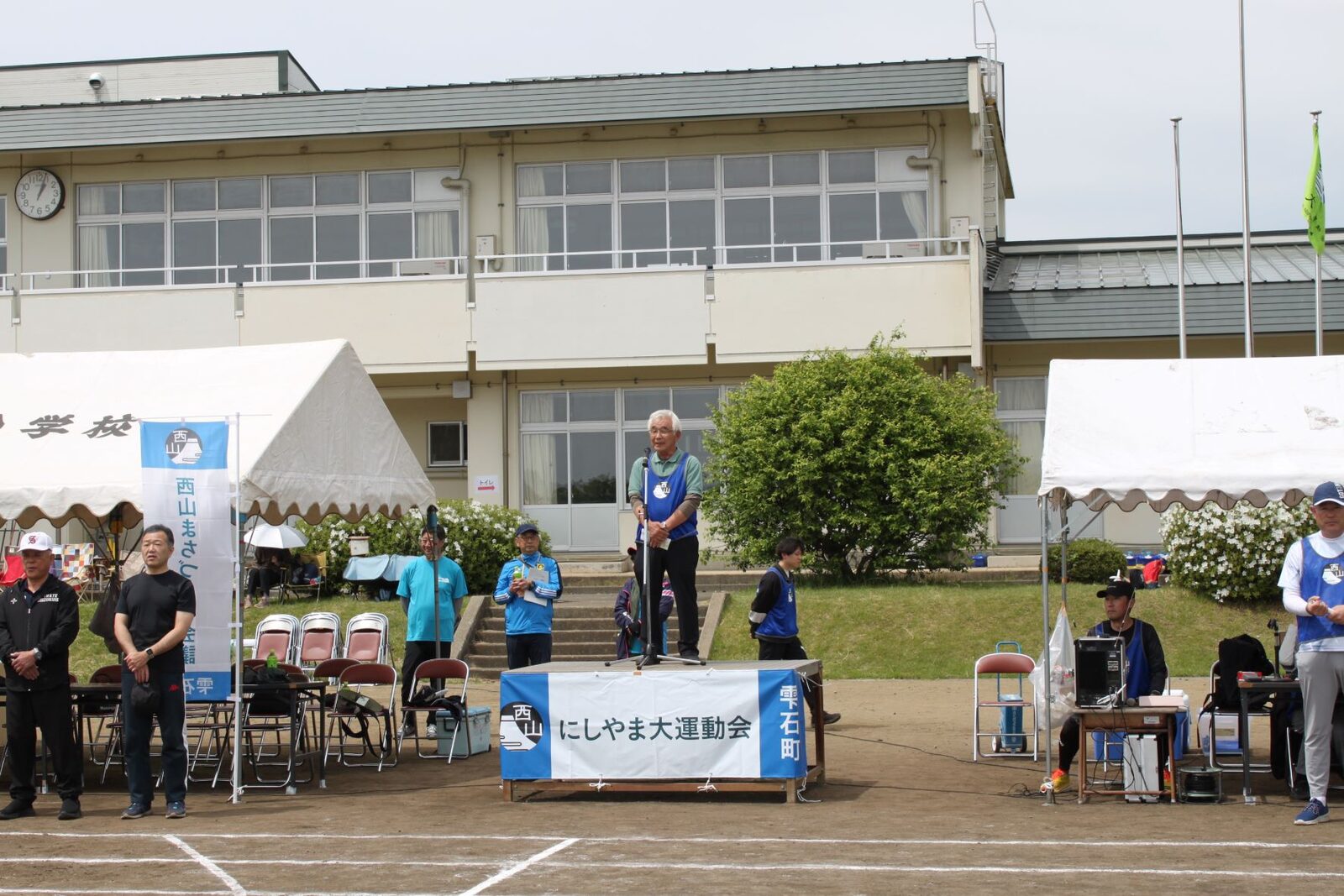 校庭に設置された演台で開会の挨拶をする様子