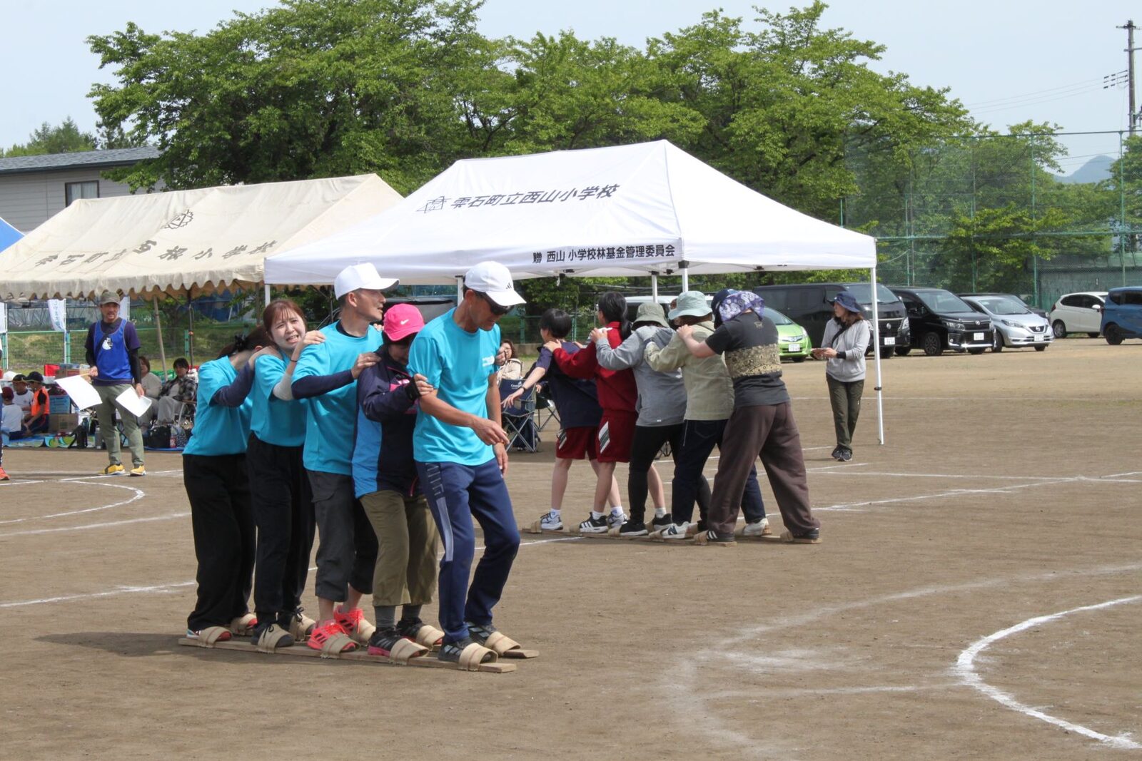 長い板の上に並んで肩を組み、息を合わせて進むムカデ競走の様子